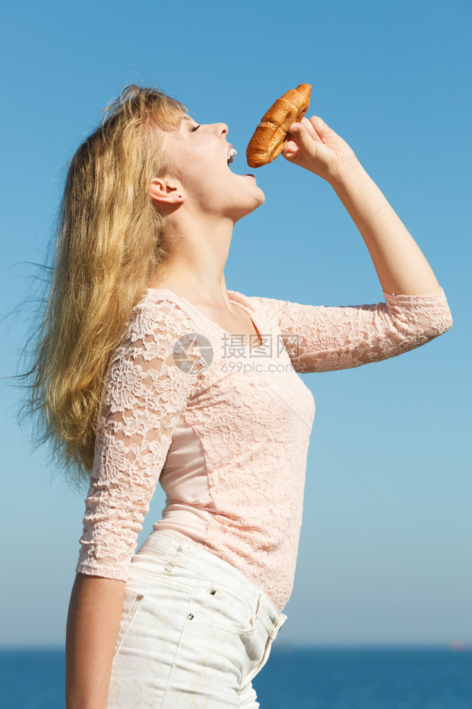 年轻女在户外吃羊角面包饭食品漂亮女孩在海边吃早餐夏天快乐年轻女在户外吃羊角面包食品图片