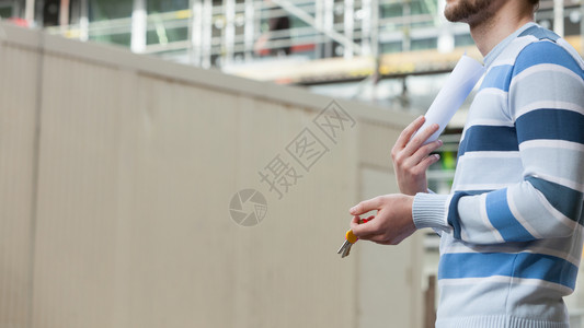 房地产概念青年男子在新的有钥匙和蓝图项目的大型现代建筑工地前图片