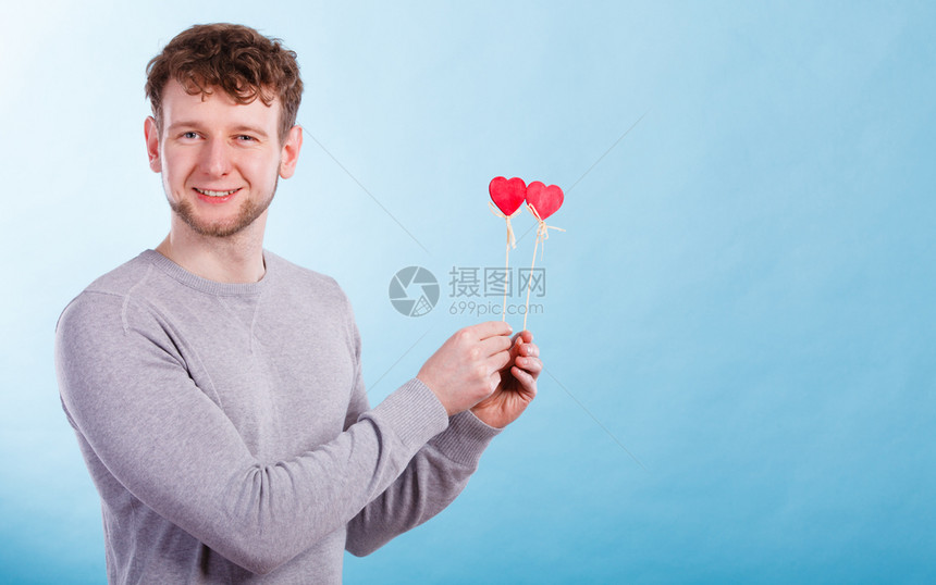 快乐的笑年轻男人用小红心在棍子上浪漫的男人梦想着他爱情关系图片