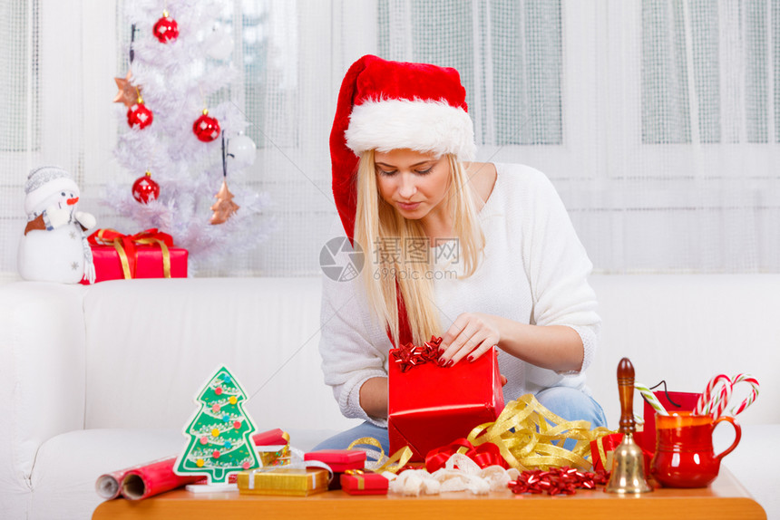 节日礼物季节概念戴圣诞帽的女人坐在沙发上打开圣诞礼物戴圣诞帽的女人打开圣诞礼物图片
