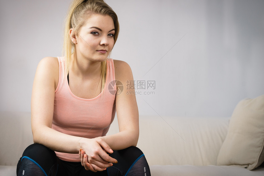 穿着运动服坐在沙发室内准备锻炼的年轻金发女子在家训练身体健康图片