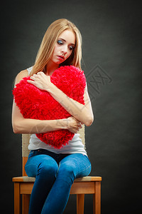伤心的坐在椅子上抱着红心枕头的不开女人黑暗背景图片