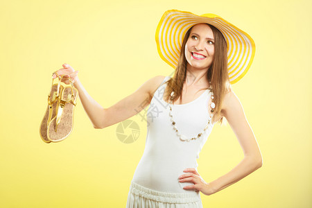 穿着大黄帽子的女人拿着金色凉鞋手边很亮图片