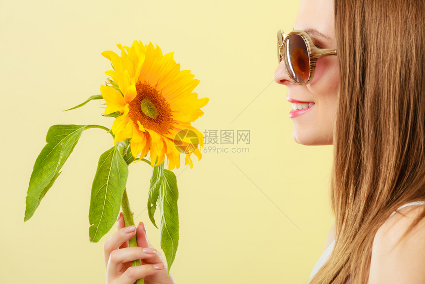 更近的一面观察着迷人的夏日女子身着太阳镜手拿向日葵背黄色景图片