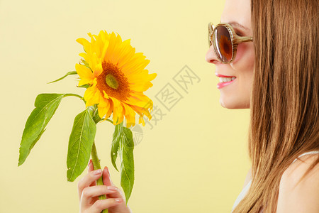 黄色太阳镜更近的一面观察着迷人的夏日女子身着太阳镜手拿向日葵背黄色景背景