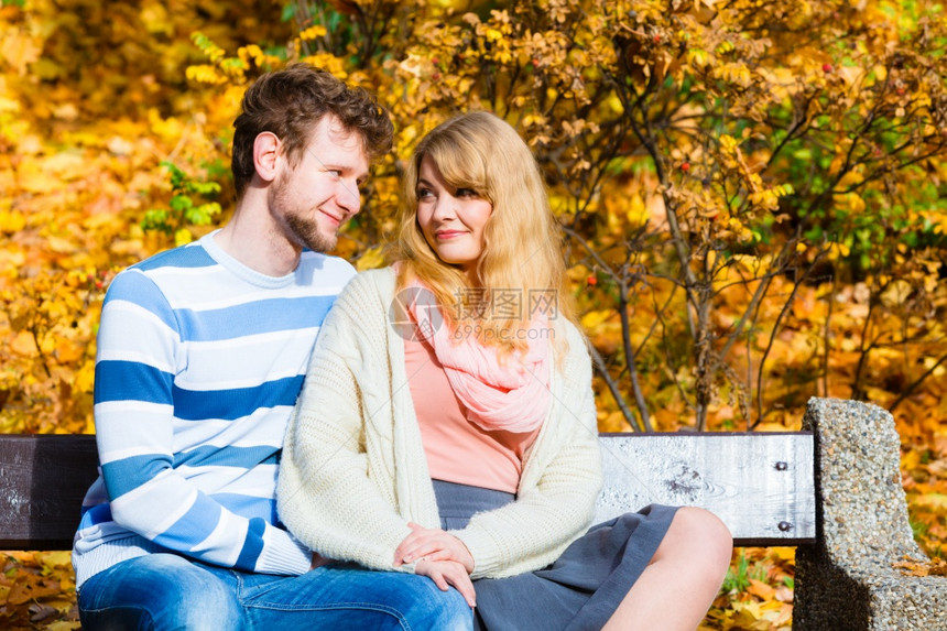 一对夫妇在秋天公园的长椅上约会图片