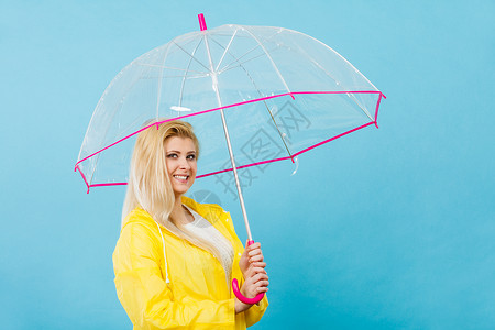 黄色的雨伞雨天时心情良好金发妇女快乐穿着黄色雨衣拿透明伞戴雨衣伞穿雨衣的妇女快乐穿着透明伞背景