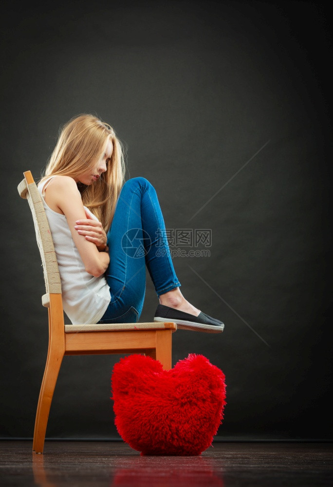 心碎的爱情概念坐在椅子上地板深底黑暗背景的红心枕头上悲哀不幸妇女图片