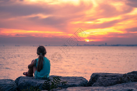 小女孩坐在岩石上看着日落图片