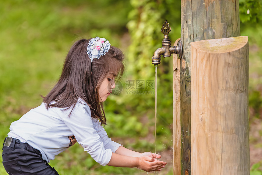 可爱的四岁小女孩在阳光明媚的一天喝着来自森林木水龙头的图片