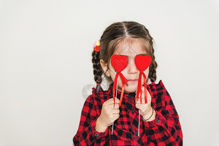 可爱的小女孩有着两件小的红色形状紧闭眼睛独身背景的假日概念穿着校服的可爱小快乐女孩的肖像背景图片