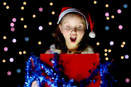 一个漂亮的小女孩打开她的圣诞礼物在黑色背景图片