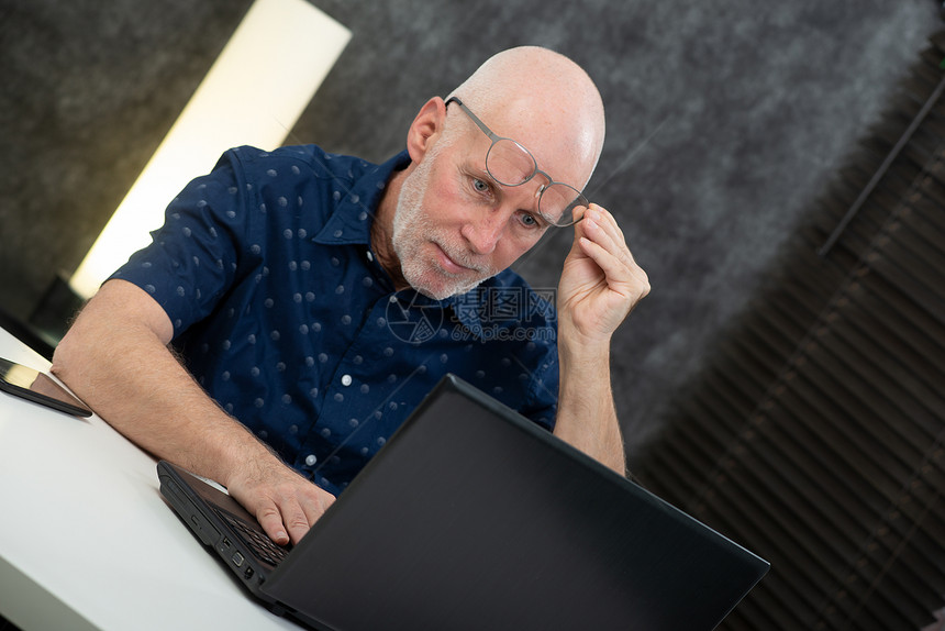 一名高级商人使用笔记本电脑有困难和视力问题图片