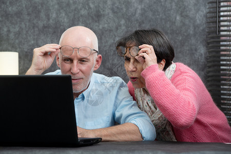 一对使用笔记本电脑的老年夫妇有困难和视力问题图片