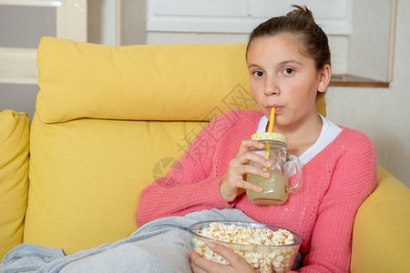 一个年轻少女坐在黄色沙发里喝橙汁图片