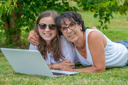 一个微笑的母亲和女儿使用笔记本电脑在花园图片