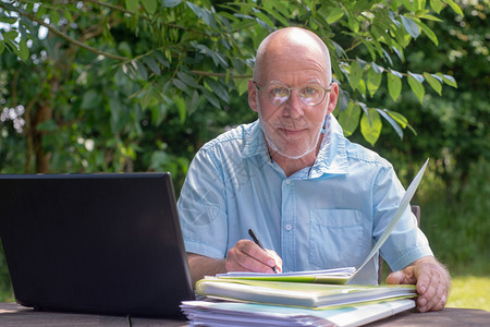 一名高级男子在花园使用笔记本电脑图片