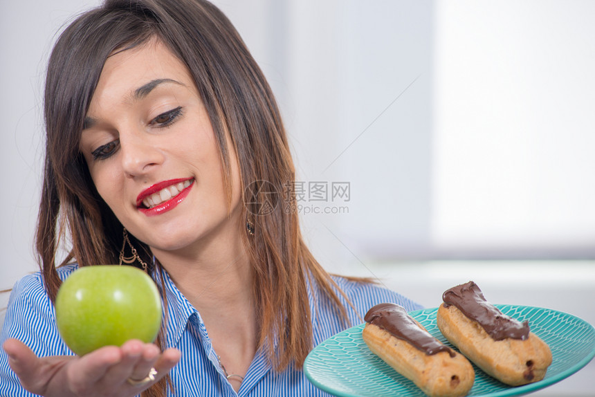 年轻女子在苹果和巧克力糕饼之间选择图片