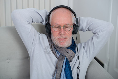 快乐的老人用耳机在家里听音乐图片