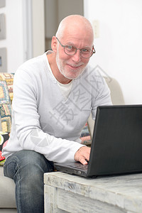 坐在沙发上用笔记本电脑工作的老年人图片