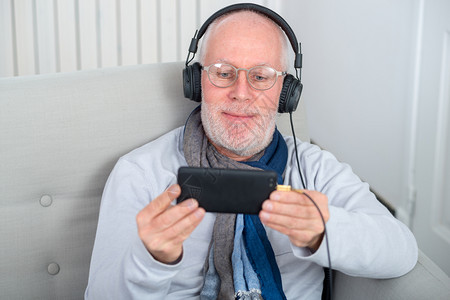 快乐的老人用耳机在家里听音乐高清图片