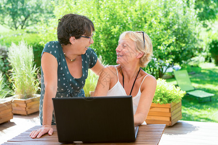 两个美丽的成熟女朋友使用笔记本电脑在花园露台图片