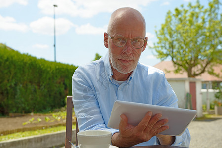 一个成熟的男人使用平板电脑坐在花园里图片
