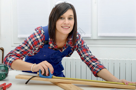 漂亮的年轻女子建筑工测量木板的图片