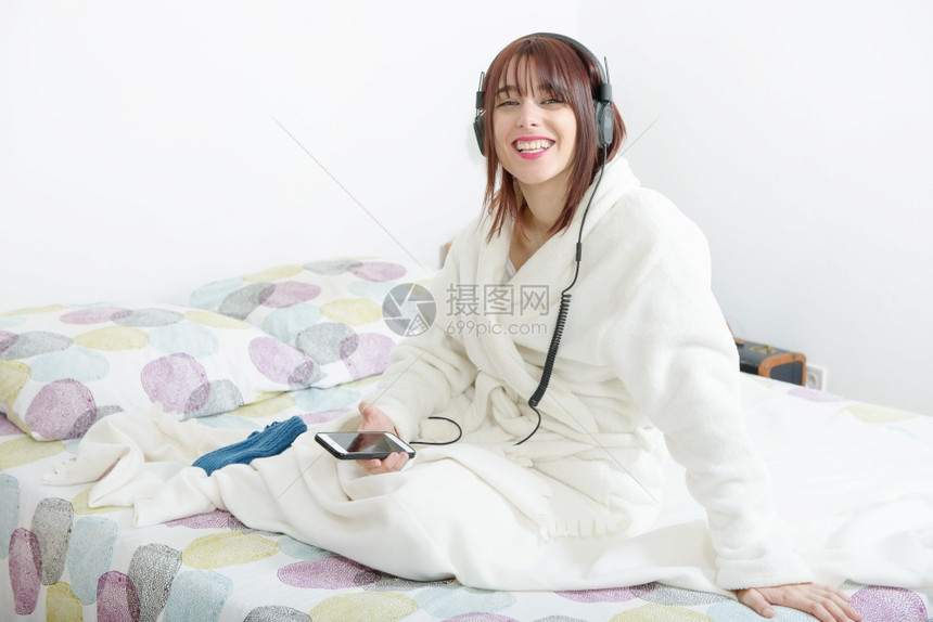 美丽的年轻女孩在床上用耳机听音乐图片