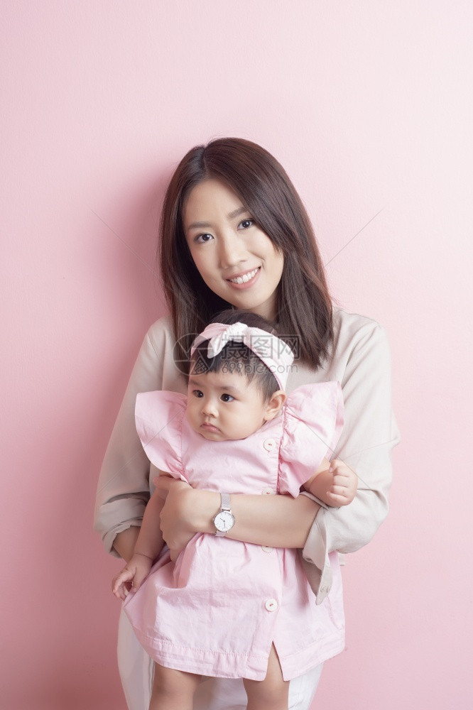 亚裔母亲和可爱的女婴以粉红背景为乐图片