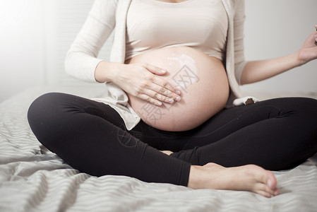 孕妇护肤品孕妇腹部涂抹乳霜的特写镜头背景