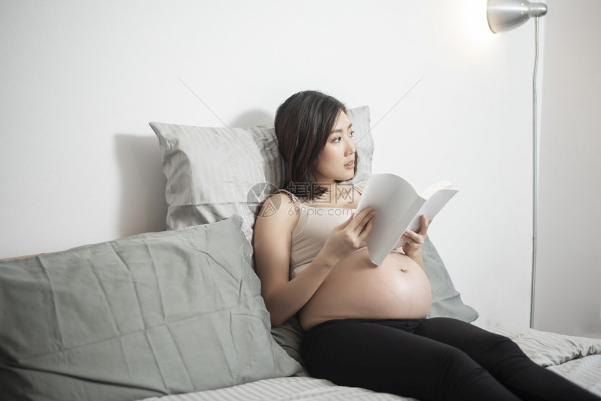 美丽的亚洲孕妇躺在床上看书图片