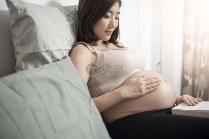 美丽的亚洲孕妇躺在床上看书图片