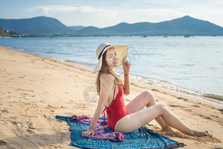 红色挂脖泳衣穿红泳衣的美女坐在沙滩上背景