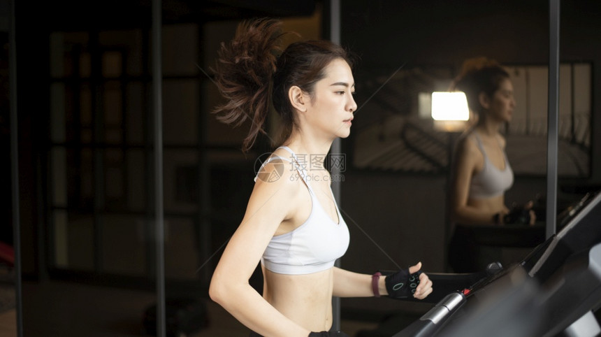 美丽的亚洲运动女员正在健身房的跑步机上图片
