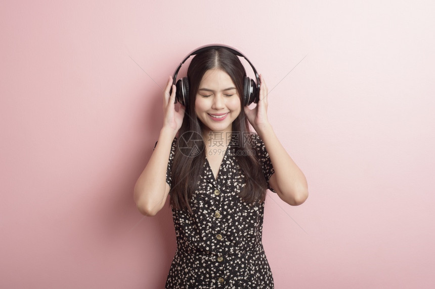 音乐情爱女人正享受着粉红色背景的耳机图片