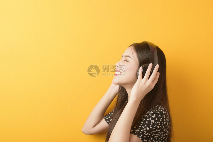 音乐情人女正享受黄色背景的耳机图片