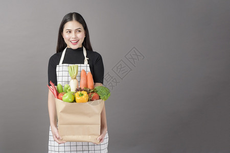 美丽的年轻女肖像蔬菜在杂货袋里灰色背景的工作室图片