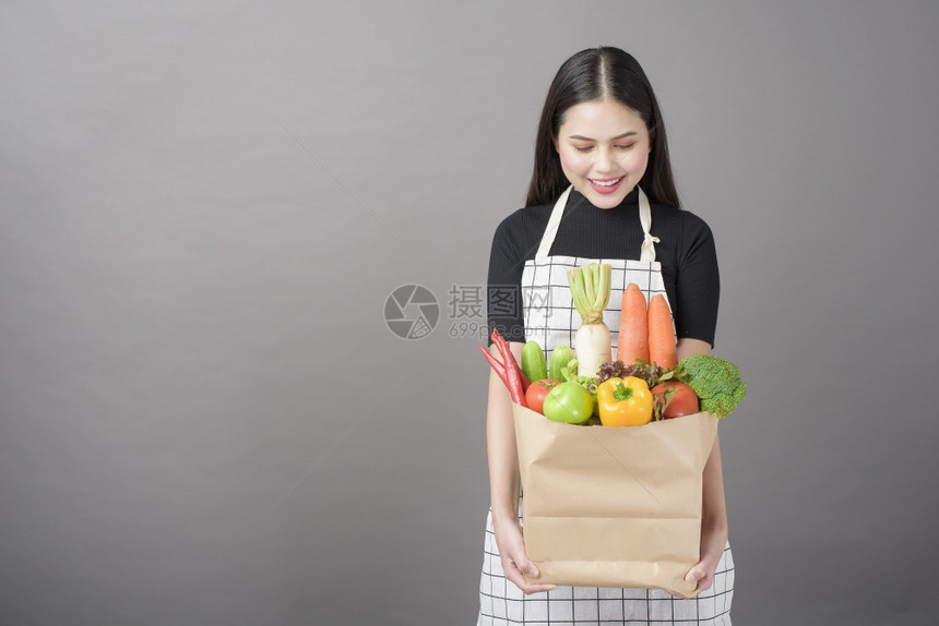 美丽的年轻女肖像蔬菜在杂货袋里灰色背景的工作室图片