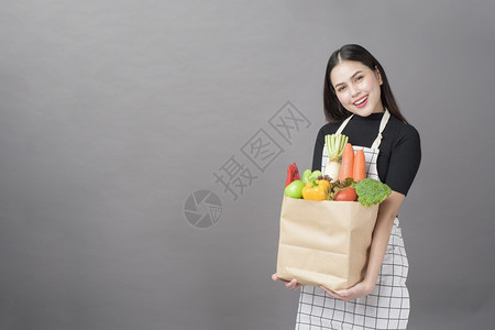 杂货系列美丽的年轻女肖像蔬菜在杂货袋里灰色背景的工作室背景