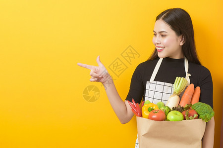 美丽的年轻女士拿着蔬菜在杂货袋黄色背景工作室黄色背景背景