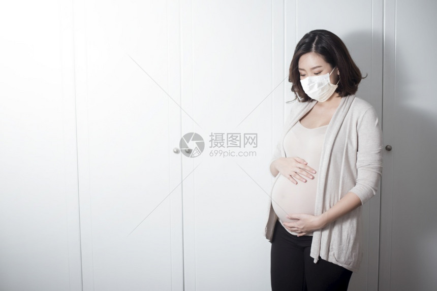 美丽的亚洲孕妇在家中戴着保护面罩图片