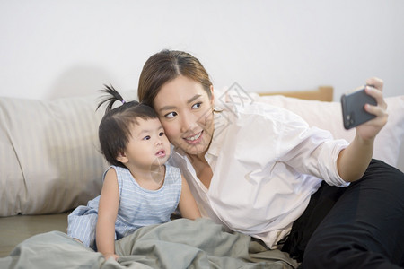 亚洲母亲及其女婴在床上家庭安全父母亲技术概念等场合向父亲打自拍或视频电话亚洲母亲及其女婴在床上技术概念等方面向父亲打自拍或视频电背景图片