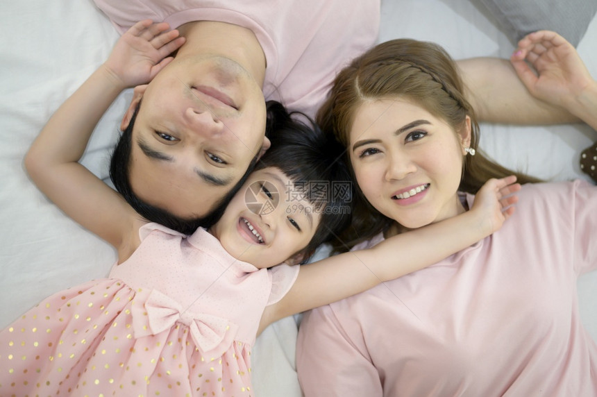 一个快乐的亚洲家庭穿着粉红衬衫肖像坐在室内白床上图片