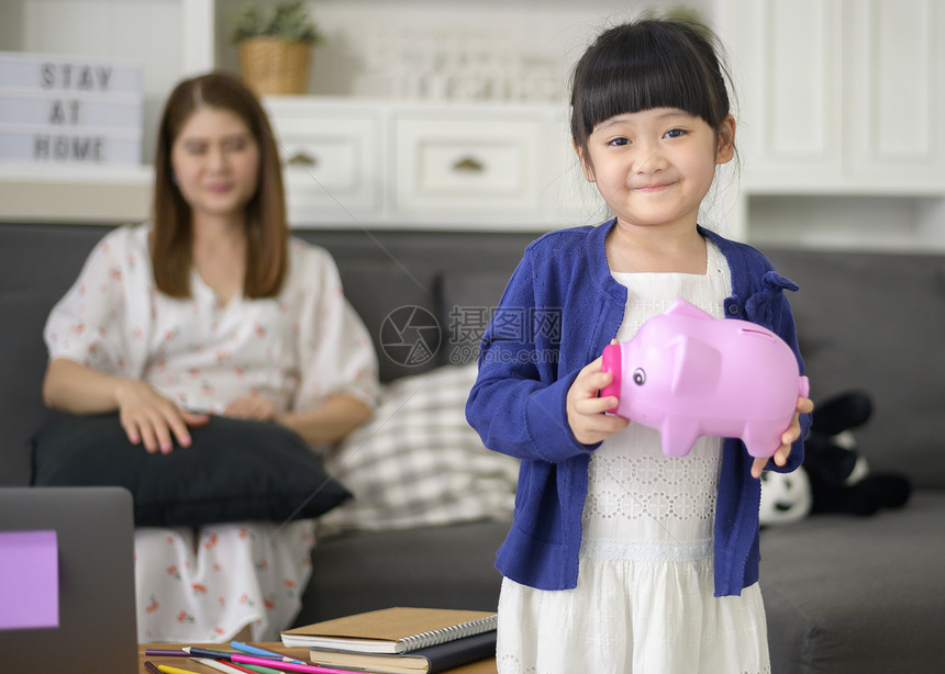 一个亚洲家庭正在用小猪银行储蓄钱教育女儿财务规划概念图片