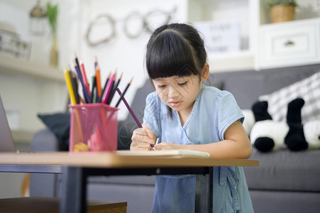 一个可爱的小女孩正在使用笔记本电脑在家中通过互联网在线学习图片