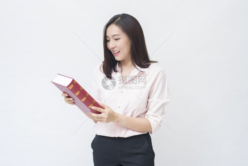 穿着粉红色衬衫的漂亮女学生肖像拿着一本在白色背景工作室被孤立的书图片