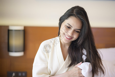 穿着白浴袍微笑的年轻女子在卧室淋浴后用毛巾洗头发图片