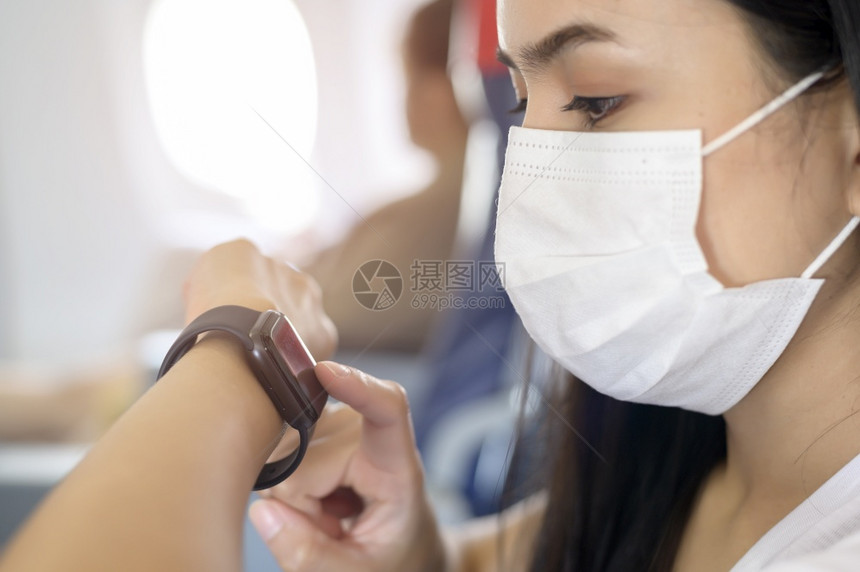 在飞机上戴口罩的女人正在使用智能手表图片