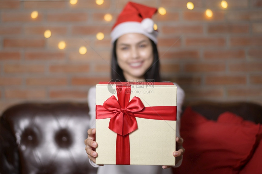 一个戴着红色圣诞老人帽子的年轻微笑女人在圣诞节时展示一个礼物盒假日概念图片